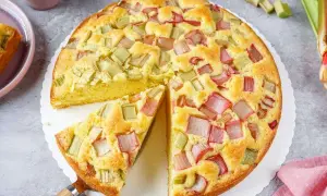 Saftiger Rhabarberkuchen in Springform, mit rosa und grünen Rhabarberstücken belegt, ein Stück herausgeschnitten.