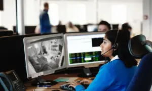 Kvinna med headset övervakar kameror på en arbetsplats, följer brandrutiner.