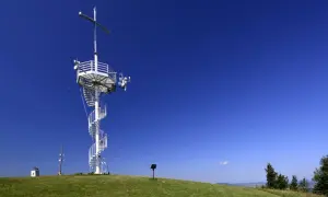 Wieża widokowa na górze Grzywackiej z kręconymi schodami i krzyżem na szczycie, na tle błękitnego nieba.