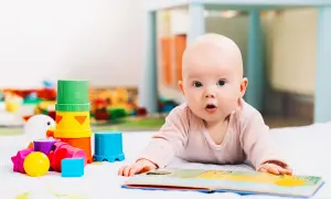 Niemowlę leży na brzuchu obok kolorowych zabawek sensorycznych i otwartej książeczki.