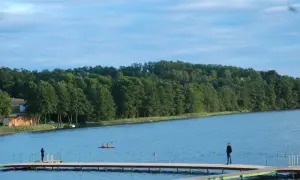 Spokojny dzień nad jeziorem Sierakowo. Ludzie spacerują po pomoście, a na wodzie pływają kajaki.