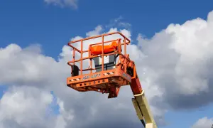 En orange korg från en JLG-lift mot en blå himmel med moln. Säkerhetsanvisningar för mobil arbetsplattform regler är synliga.