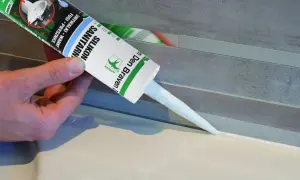 Ręka trzyma tubkę silikonu sanitarnego, aplikując go wzdłuż krawędzi zlewu, pokazując jak uszczelnić zlew.