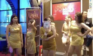 Kobiety w złotych sukienkach pozują przed banerem "Pacha". W tle neonowy napis "Shots". To scena z nocnego życia, być może związana z ping pong show w Tajlandii.