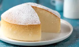 Una soffice torta nuvola, cosparsa di zucchero a velo, su un piatto bianco. La sua consistenza leggera invita a un morso goloso.
