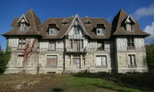 Maison abandonnée en Normandie, typique de l'urbex. Façade en colombage et pierre, toiture pentue, fenêtres brisées.