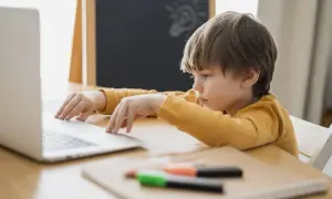 Chłopiec z problemami z koncentracją u dziecka siedzi przy laptopie, zamyślony. Na tablicy rysunek żarówki.