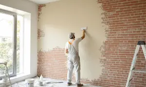 Un ouvrier applique un enduit sur brique intérieur, transformant un mur brut en une surface lisse et prête à être peinte.