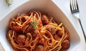 Spaghetti z klopsikami w sosie pomidorowym, udekorowane gałązką tymianku.