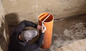 Mann markiert Rohr für Pumpensumpf im Keller.