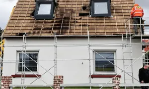 Gerüst am Haus, Dach wird saniert. Ein Arbeiter in Warnweste prüft die Arbeiten. Wer kontrolliert Sanierungspflicht?