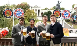 Vier FC Bayern Spieler in Tracht mit Bierkrügen, vor Paulaner- und FC Bayern-Logos. Ein Fest für alle Fans bei Veranstaltungen in Bayern.