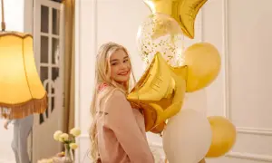 Uśmiechnięta blondynka z bukietem złotych i białych balonów w kształcie gwiazd i kuli.