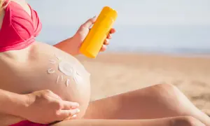 Mujer embarazada en la playa aplica protector solar en su barriga, dibujando un sol. Cuidando su piel durante el embarazo.