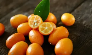 Kumkwat jak smakuje? Te małe, pomarańczowe owoce na drewnianym tle kuszą słodko-kwaśnym smakiem. Jedz je w całości, ze skórką!