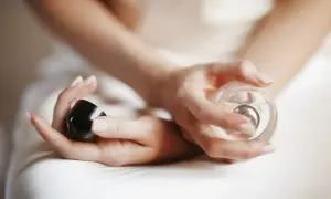Dłonie kobiety trzymają flakon perfum i czarną nakrętkę. Chcesz wiedzieć, gdzie sprawdzić kod perfum?