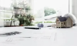 Na stole architekta: makieta domu, cyrkiel, ołówki i plany, które wyznaczają nieprzekraczalna linia zabudowy.