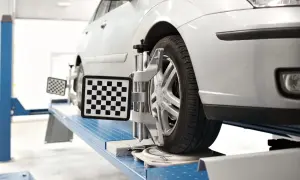 Ein Auto auf einer Hebebühne, dessen Räder mit Messgeräten für die Achsvermessung ausgestattet sind. Der Sturz wird präzise eingestellt.