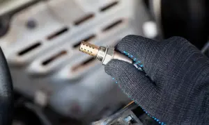 Hand in a glove holds a new auto lambdasonde, ready for installation in a car engine.