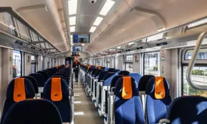 Wnętrze pociągu Intercity. Widok na rzędy niebieskich siedzeń z pomarańczowymi zagłówkami. Czym się różni 1 klasa od 2 w pociągu Intercity?