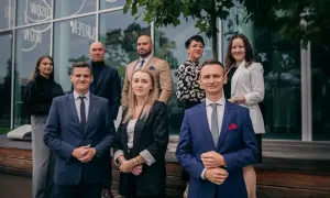 Grupa profesjonalistów w garniturach i eleganckich strojach pozuje przed nowoczesnym budynkiem.