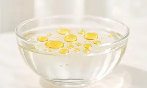 Gocce dorate di olio feci che galleggiano sulla superficie di un liquido trasparente in una ciotola di vetro.