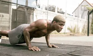 Un homme musclé s'entraîne en extérieur, effectuant des pompes dans un style calisthenics militaire.