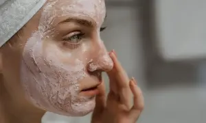 Kobieta z maską na twarzy, walcząca z nadmiarem sebum. Delikatnie dotyka nosa, aplikując kosmetyk.