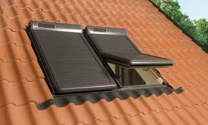 Dwa ciemne rolety zewnętrzne na okna dachowe, jeden częściowo otwarty, na tle pomarańczowej dachówki.