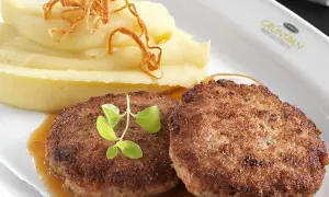 Zwei saftige faschierte Laibchen mit cremigem Kartoffelpüree und knusprigen Röstzwiebeln, garniert mit frischen Kräutern.