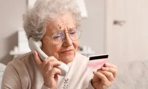 Une femme âgée, sous curatelle renforcée, semble inquiète en tenant une carte bancaire tout en parlant au téléphone.