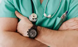 Fizjoterapeuta w zielonym fartuchu ze stetoskopem i zegarkiem na ręce.