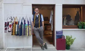 Uomo con metro da sarto nel suo atelier a Venezia. Borse colorate in esposizione.