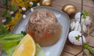 Tradycyjne zimne nóżki przepis babci, galareta z mięsem i marchewką, ozdobiona cytryną i sałatą. W tle wielkanocne jajka.