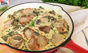 Miękkie polędwiczki wieprzowe w sosie grzybowym, udekorowane koperkiem. Pyszne danie w czerwonej patelni.