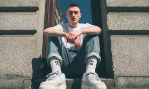 Młody mężczyzna w jeansach i białej koszulce prezentuje modne **wysokie skarpetki stylizacje**.
