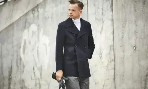 Elegancki mężczyzna w granatowej bosmance i białym golfie, trzymający czarne rękawiczki.