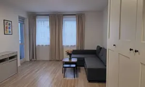 Nowoczesny salon z szarą kanapą, stolikiem kawowym z kwiatami i dużymi oknami.