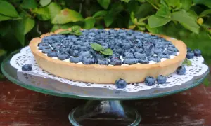 Pyszna tarta z borówkami, udekorowana listkami mięty, prezentuje się apetycznie na szklanej paterze.