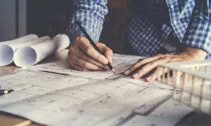 Architetto disegna progetto, con rotoli di carta e modello edilizio. Lavora per ottenere il permesso di costruire in sanatoria.