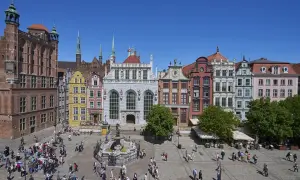 Tętniący życiem gdański plac z Dworem Artusa, fontanną Neptuna i kolorowymi kamieniczkami.