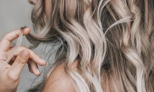 Dłoń dotyka falujących włosów w odcieniu sombre blond, podkreślając ich naturalne przejścia kolorystyczne.