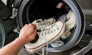 Mano che inserisce scarpe da ginnastica bianche in lavatrice per lavarle. La centrifuga le renderà come nuove!