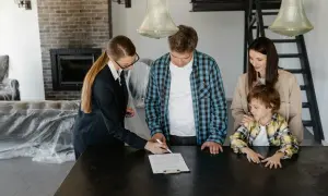 Rodzina podpisuje dokumenty dotyczące darowizny mieszkania. Kobieta w garniturze wskazuje miejsce do podpisu.