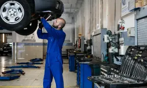 Mécanicien en bleu travaillant sous une voiture. Outils visibles, suggérant le prix de la main d'œuvre de garage.