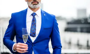 Elegancki mężczyzna w niebieskim stroju koktajlowym z wzorzystym krawatem trzyma kieliszek szampana.