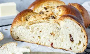Ein goldbrauner Hefezopf mit Rosinen, frisch gebacken und bereit zum Genießen. Daneben liegt ein Stück Butter.