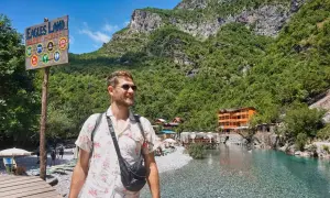 Ein Mann genießt die atemberaubende Landschaft Albaniens. Ein Schild weist auf "Eagles Land Guest House" hin, ein perfektes Ziel für Backpacking in Albanien.
