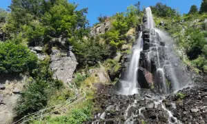 Der Trusetaler Wasserfall stürzt über schwarze Felsen in die Tiefe. Ein weißer Geländerweg führt Besucher am grünen Hang entlang.