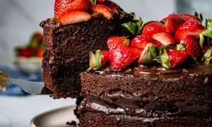 Ein hoher Schokokuchen mit frischen Erdbeeren und Schokoladenglasur wird angeschnitten.